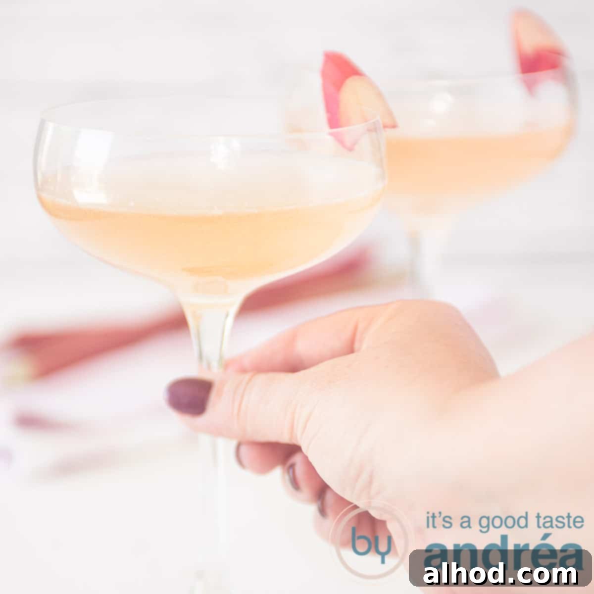 Rhubarb Champagne Sparkler 6 A square photo with two glasses filled with champagne and rhubarb syrup. A hand takes the glass