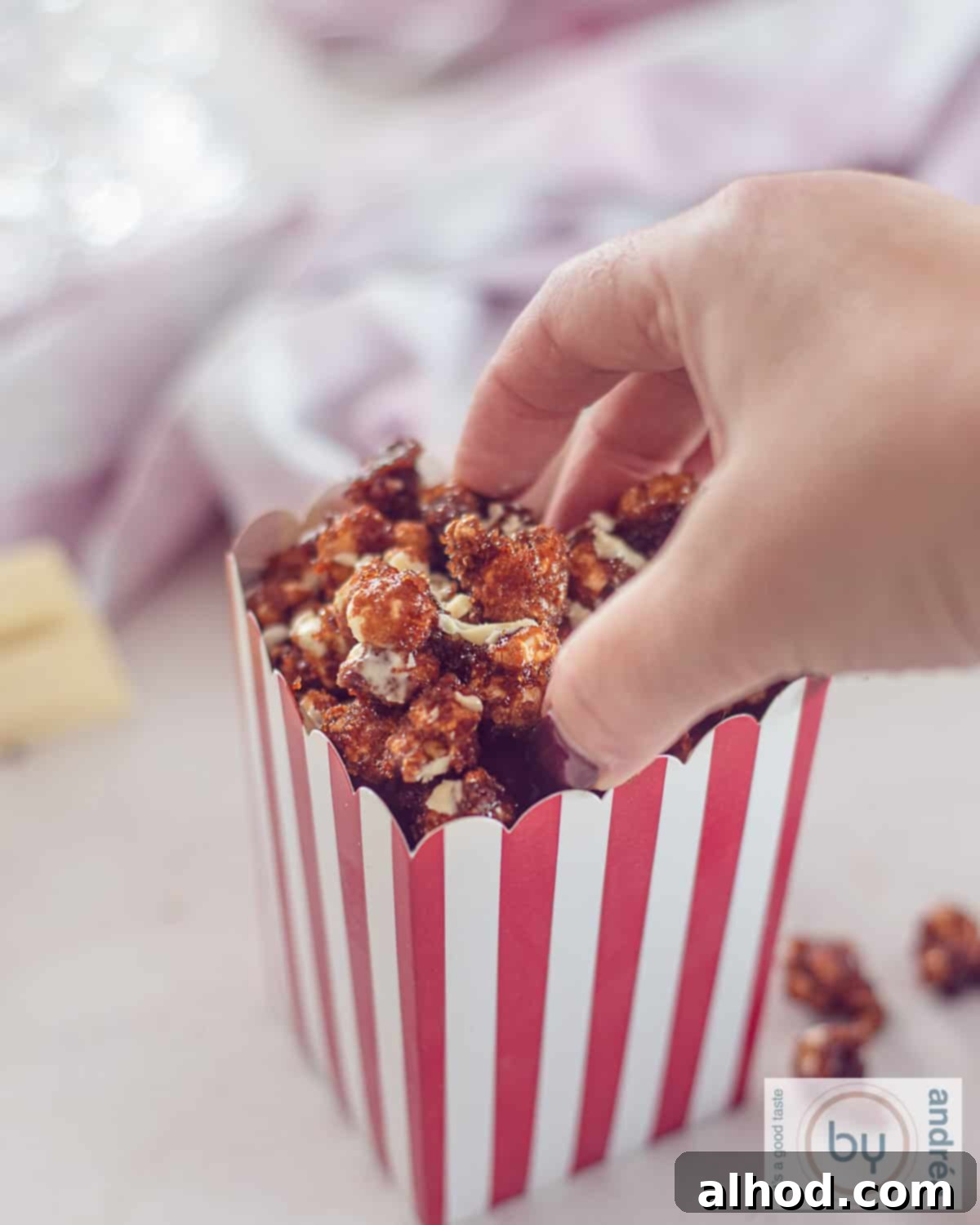 Gourmet White Chocolate Caramel Popcorn 3 A hand reaches into a rustic metal container, picking up a handful of delicious homemade caramel popcorn coated with delicate white chocolate shavings.