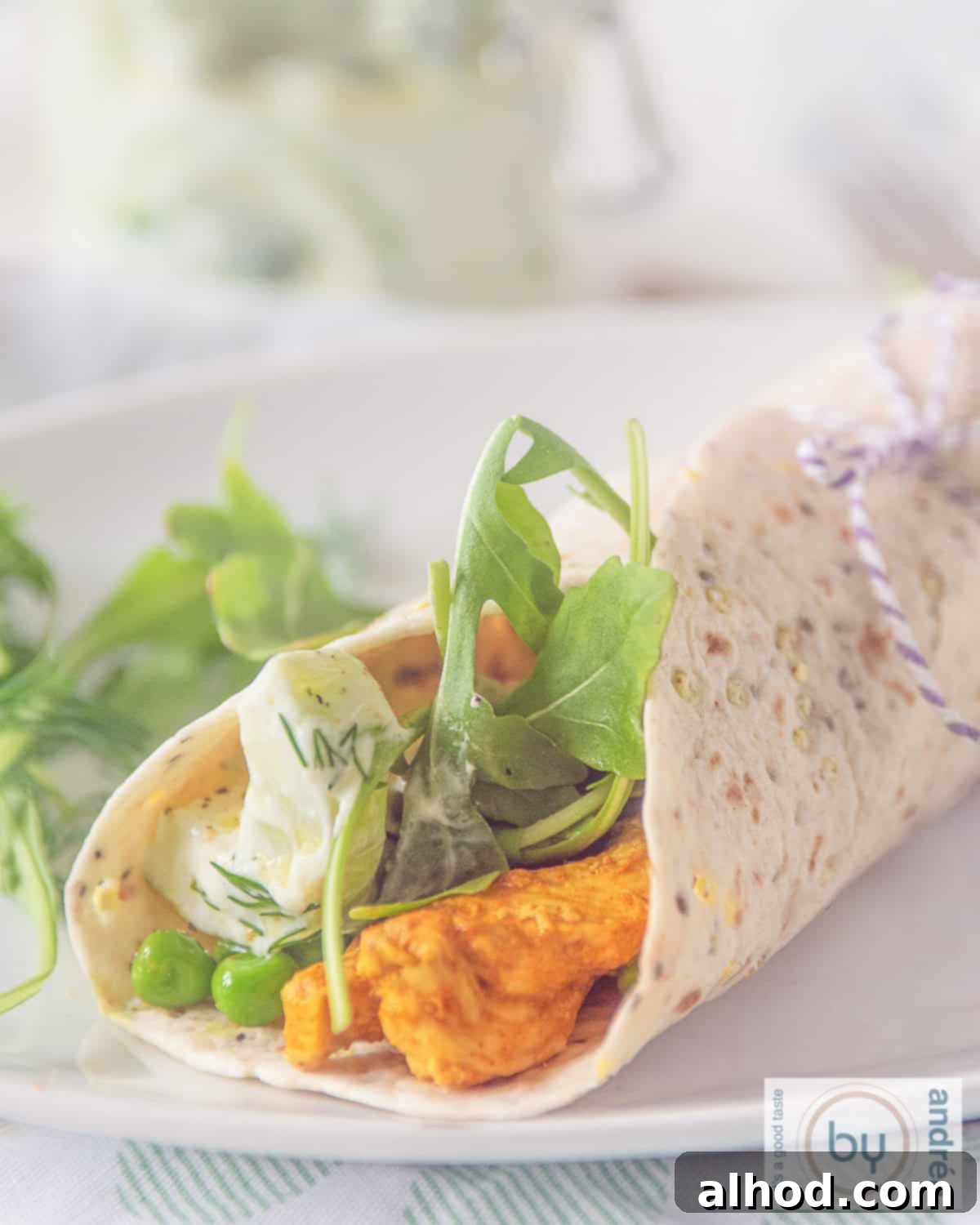 Freshly prepared Tandoori Chicken Wrap with vibrant arugula and creamy tzatziki on a white plate, ready to be enjoyed.