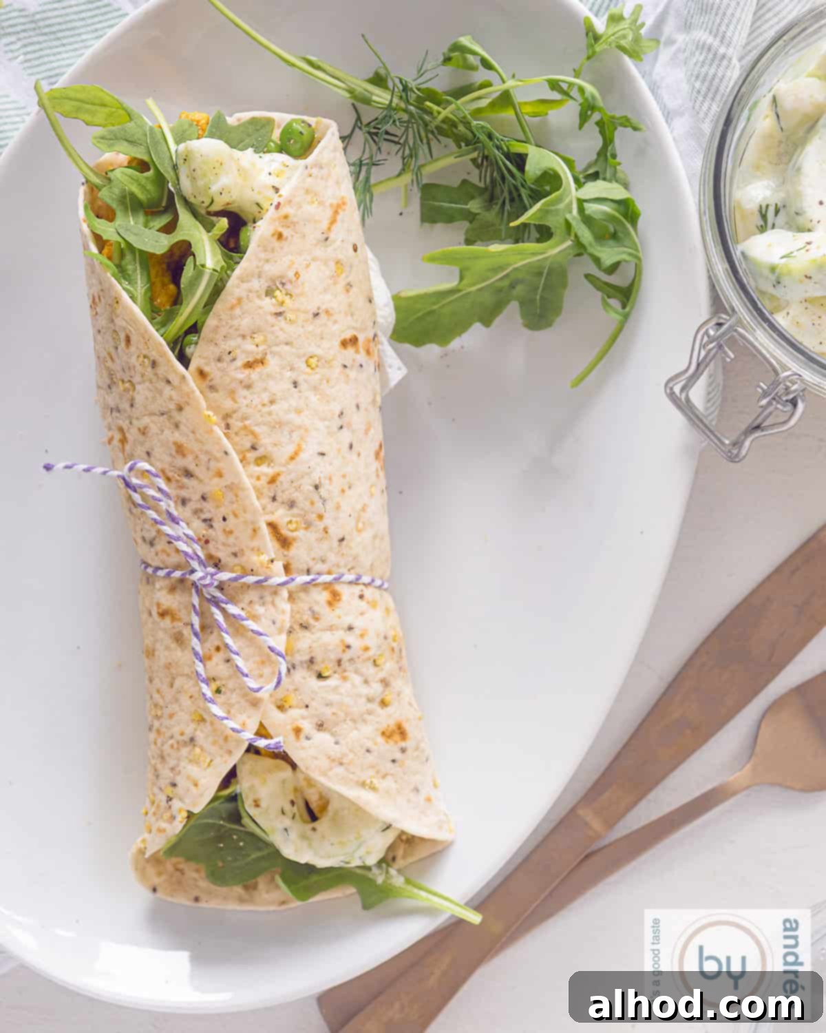 An overhead view of a beautifully rolled tortilla wrap, revealing layers of Tandoori chicken, fresh vegetables, and creamy tzatziki filling.