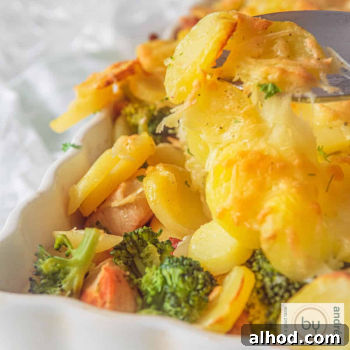 Hearty Chicken Broccoli Potato Casserole 4 A square photo with part of a white baking dish. A top layer of gratinated potatoes. Below that you see broccoli and chicken.