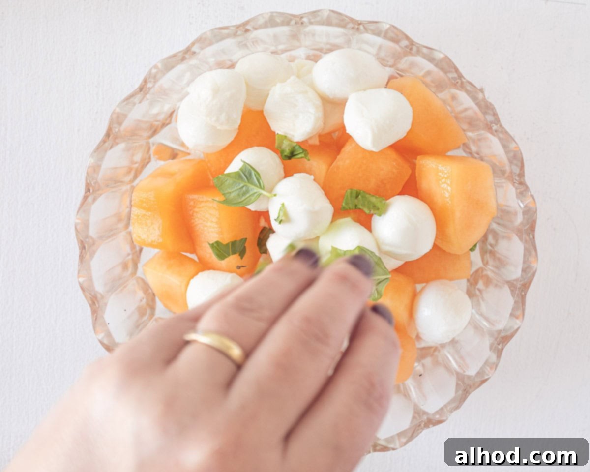 Vibrant Melon & Prosciutto Salad with Creamy Mozzarella 5 A glass bowl with cantaloupe melon cubes, mozzarella balls and basil.