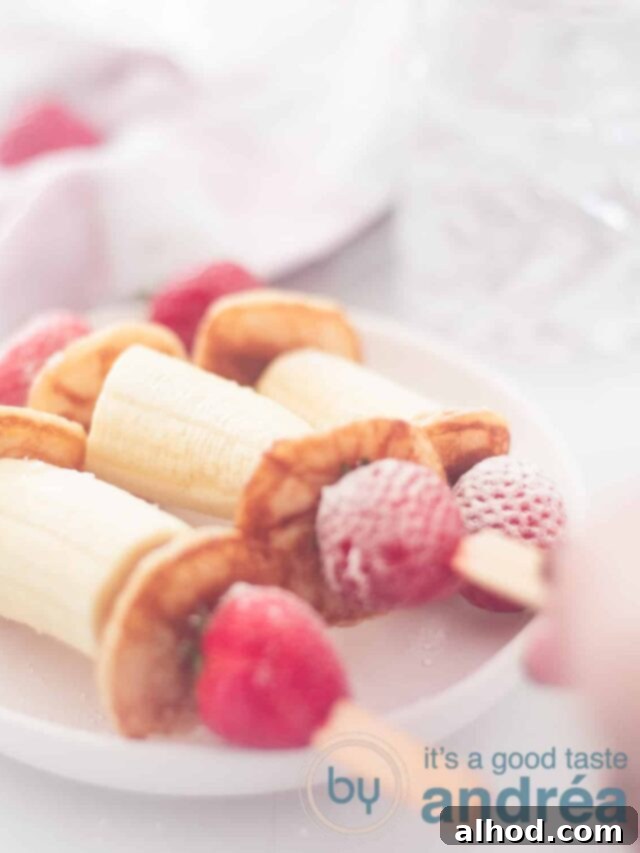 Strawberry Banana Pancake Sticks 5 3 banana strawberry poffertjes treat on a white plate. A hand takes one away.