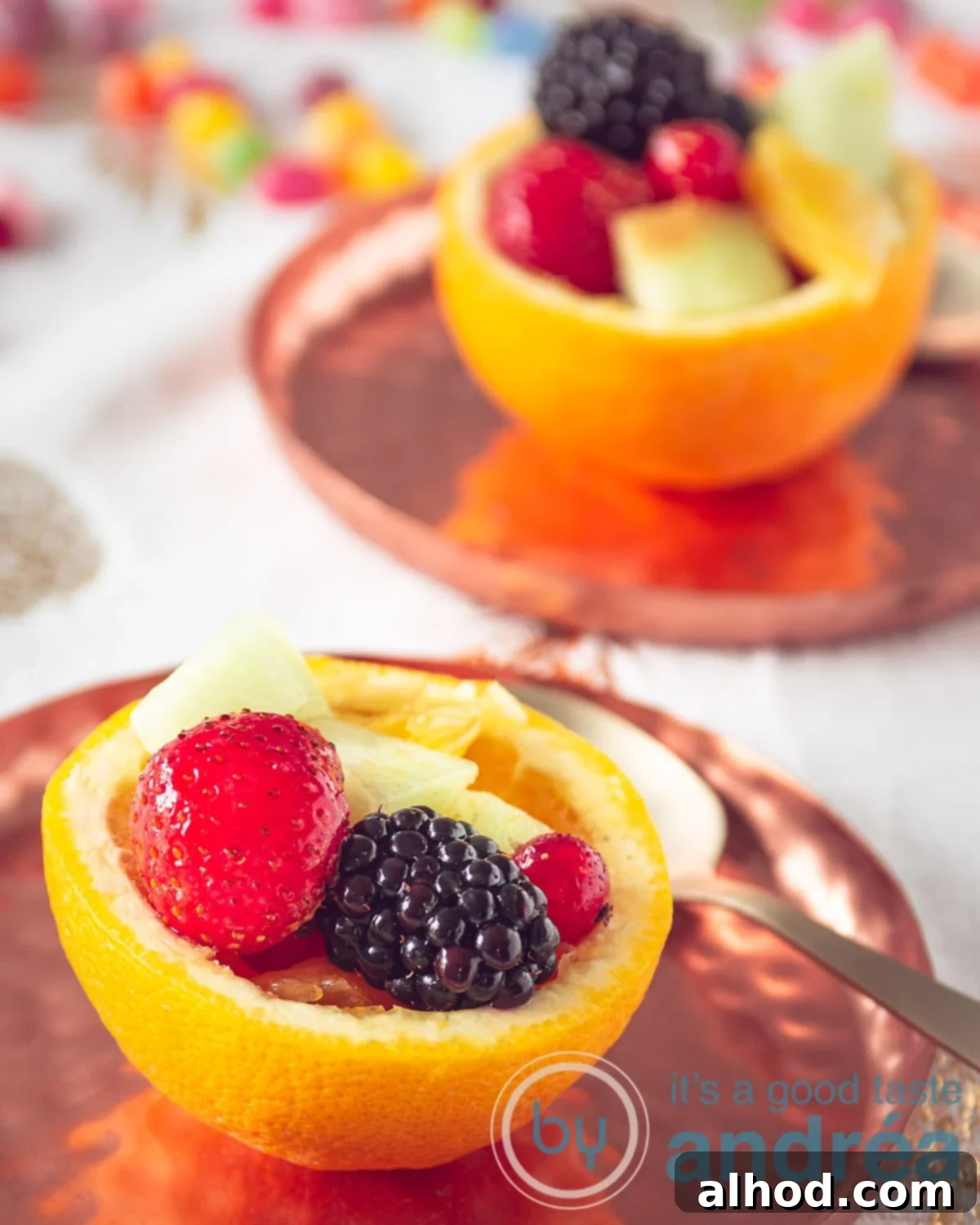 two orange bowls filled with fresh fruit on copper plates