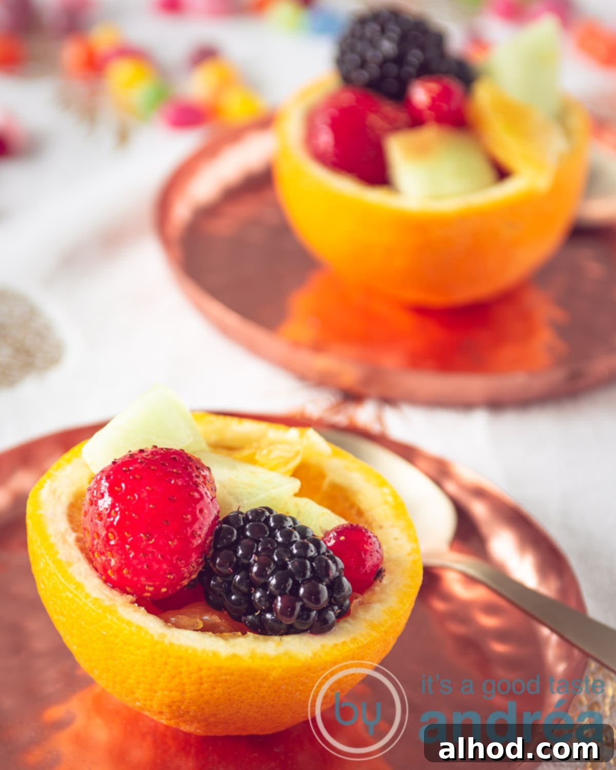 Two vibrant orange bowls brimming with a fresh, colorful fruit salad, presented on elegant copper plates.