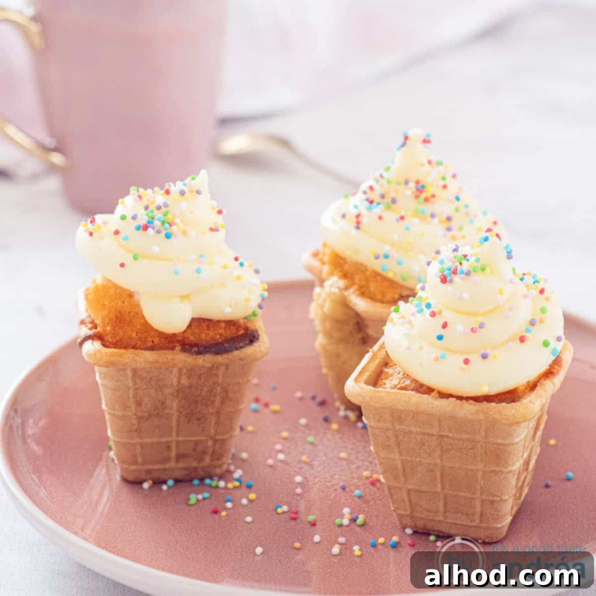 A square photo showcasing three charming ice cream cone cupcakes, beautifully decorated with frosting and presented on a pink plate.