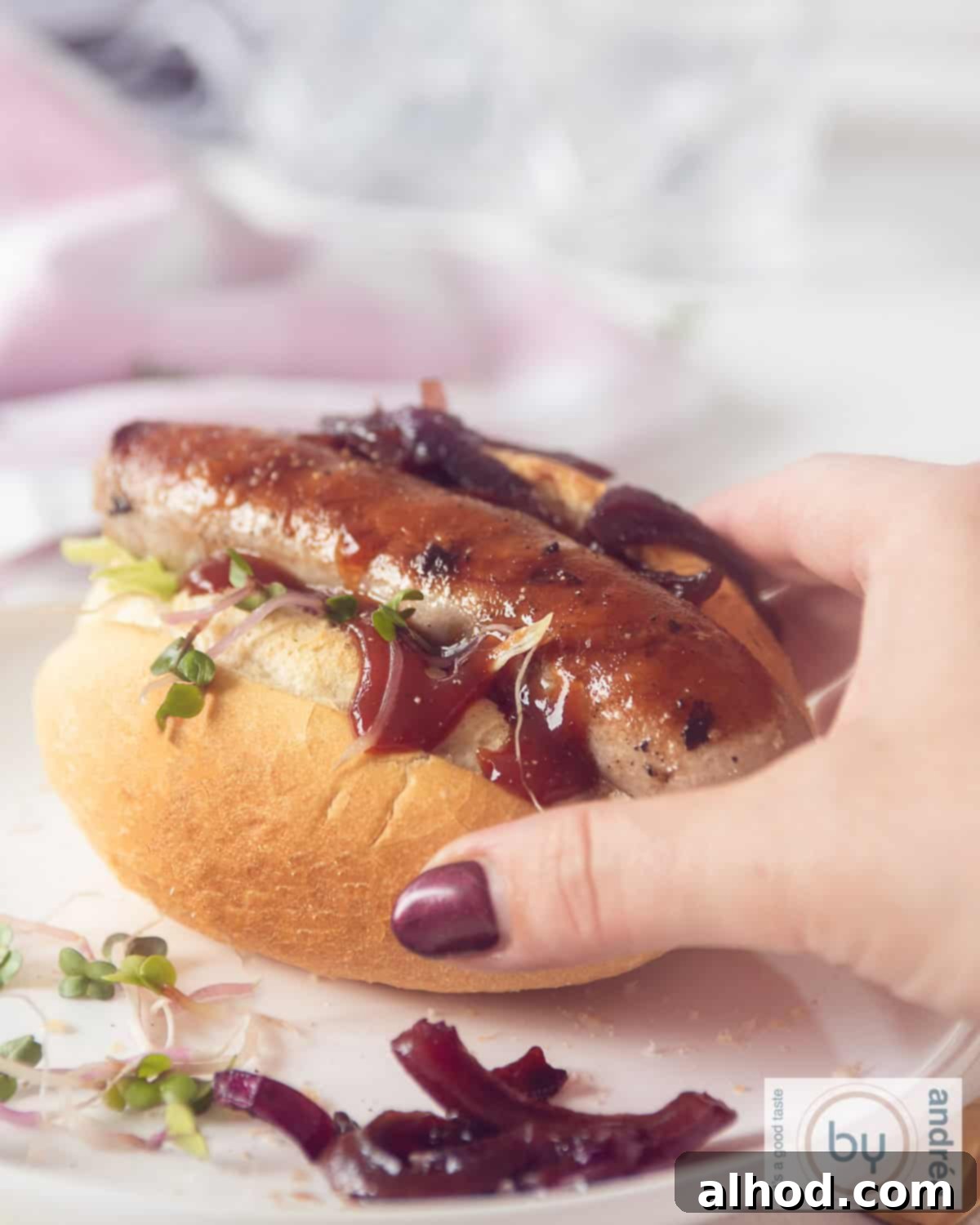 Grilled Beer Brats Crowned with Sweet Caramelized Onions 3 Bratwurst from the bbq on a bun with ketchup. A hand taken hte bun