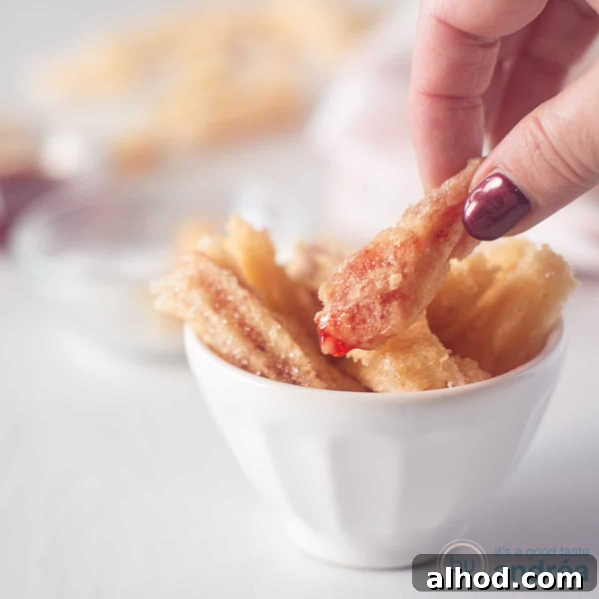 Strawberry Burst Churros 4 A square photo with a white bowl filled with strawberry churros. A hand grabbed a churro.