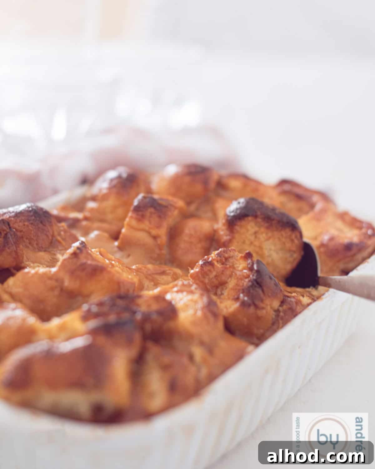 Decadent Dulce de Leche Bread Pudding 2 A height photo of a white baking dish filled with caramel bread pudding. A spoon takes a bite