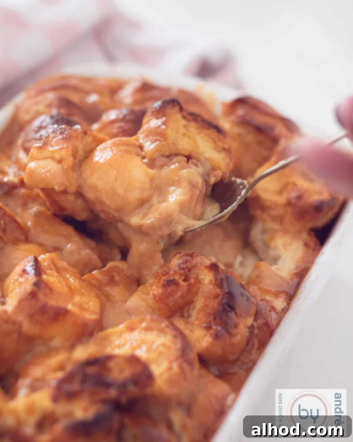Decadent Dulce de Leche Bread Pudding 3 A height photo with an oven dish filled with brioche and sweet caramel sauce. A spoon takes a shovel