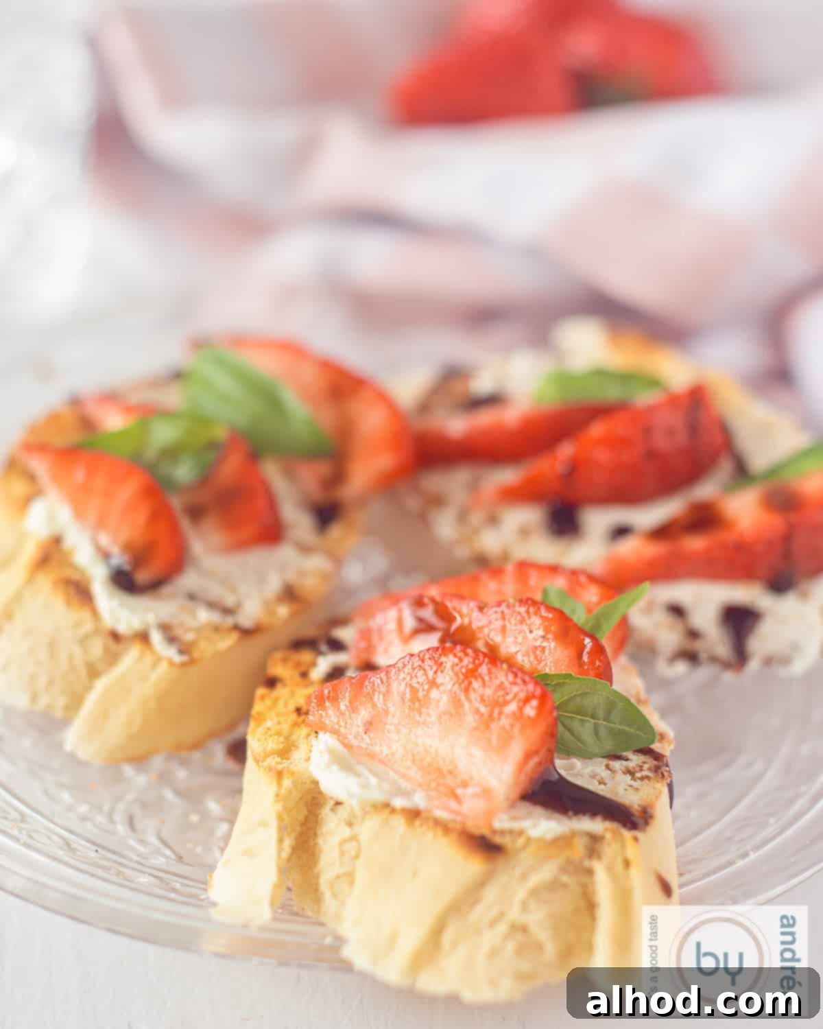 A height picture with three slices of baguette, grilled and topped with strawberries, basil, balsamic and mascarpone on a glass plate