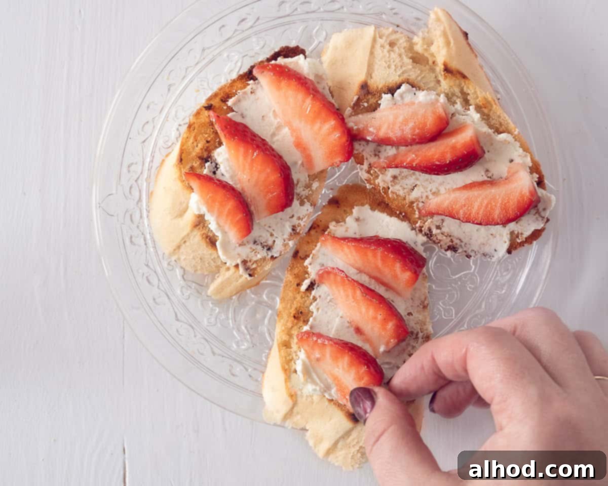 A glass plate with three baguette slices smeared with mascarpone and topped with strawberries