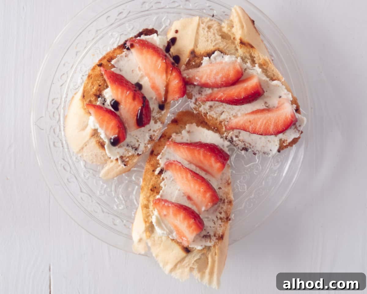 Three bruschetta on a glass plate on a white background topped with mascarpone, strawberries and a drizzle of balsamic glaze