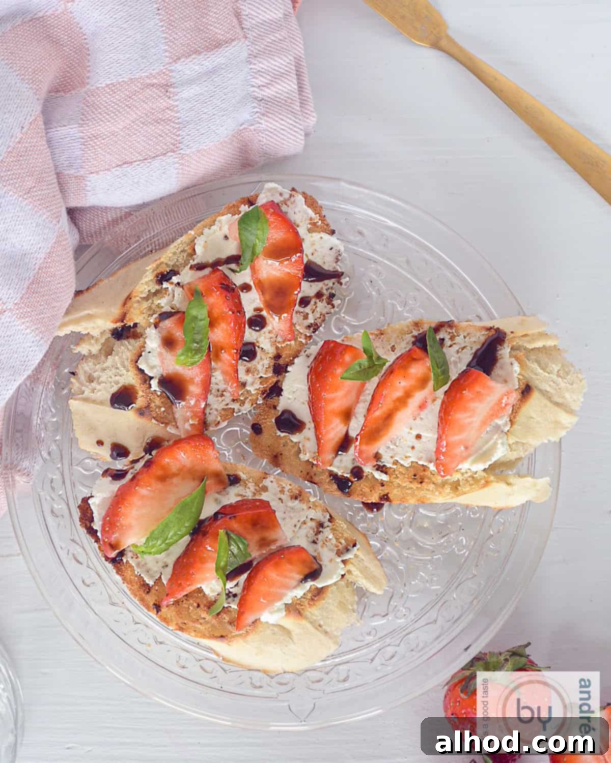 A height photo, top down of a glaze plate on a white background. Three balsamic strawberry bruschetta on top. A pink/white cloth in the left corner.