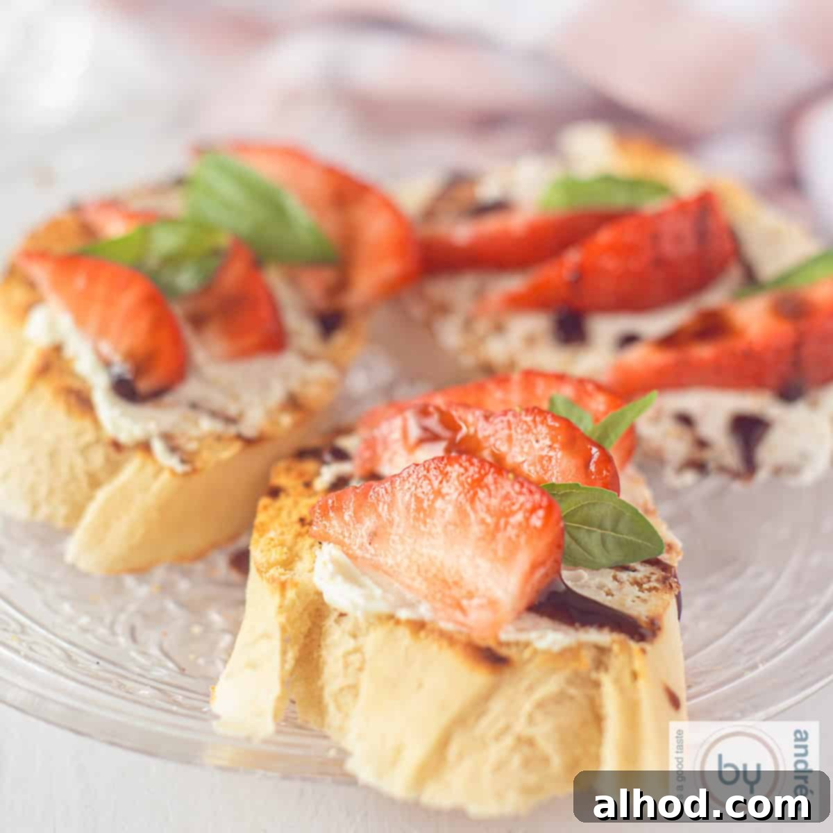 A square picture of a glass plate with three bruschetta with mascarpone, balsamic, strawberries and basil.