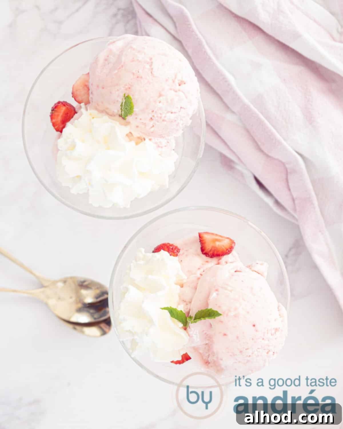 Easy No Churn Strawberry Ice Cream 2 A photo from above with two glas bowls filled with scoops no churn strawberry ice cream, fresh strawberries, whipped cream and mint. To the right a white pink towel. Left two golden spoons