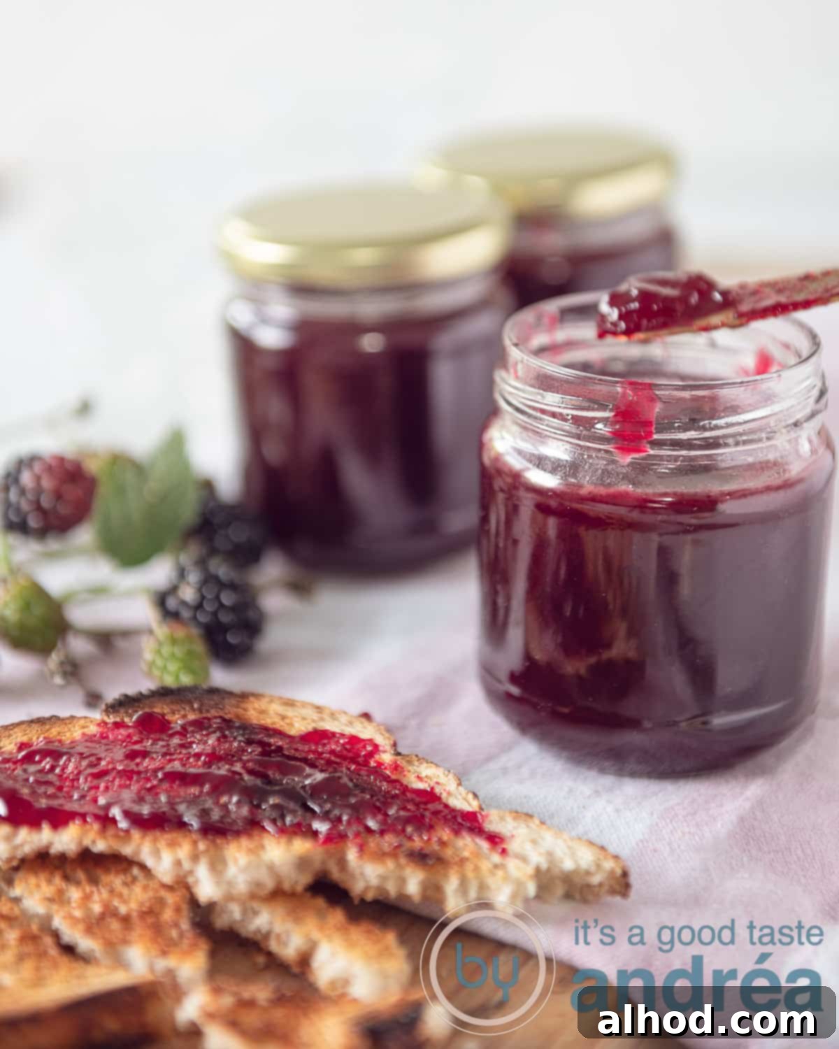An elevation photo with three jars of jam, 1 of the jars is open and jam is being removed from there. Front left three slices of bread spread with jam