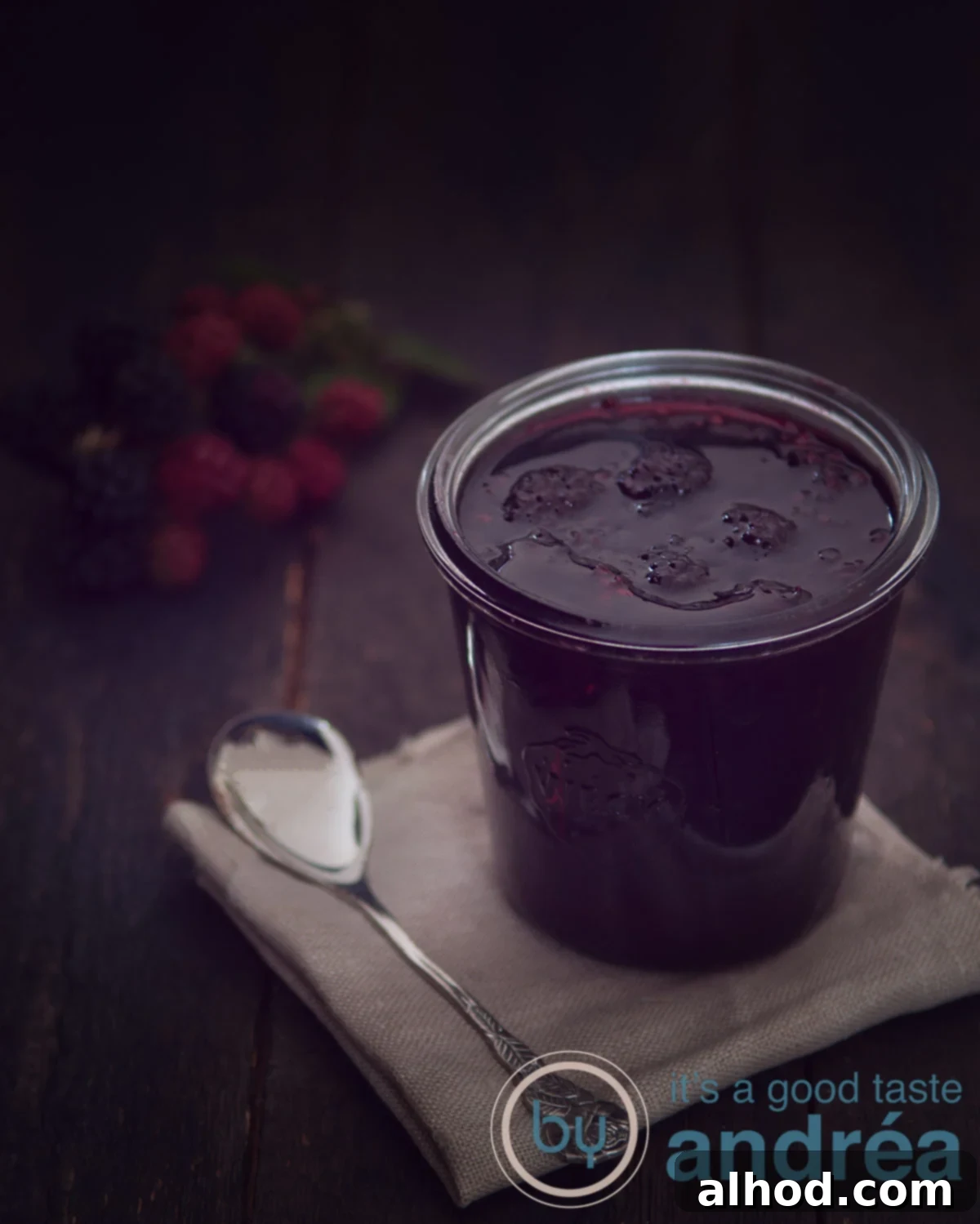 Aromatic Blackberry and Oregano Jam 5 Blackberry jam with oregano on a brown cloth a spoon on the left on a black background