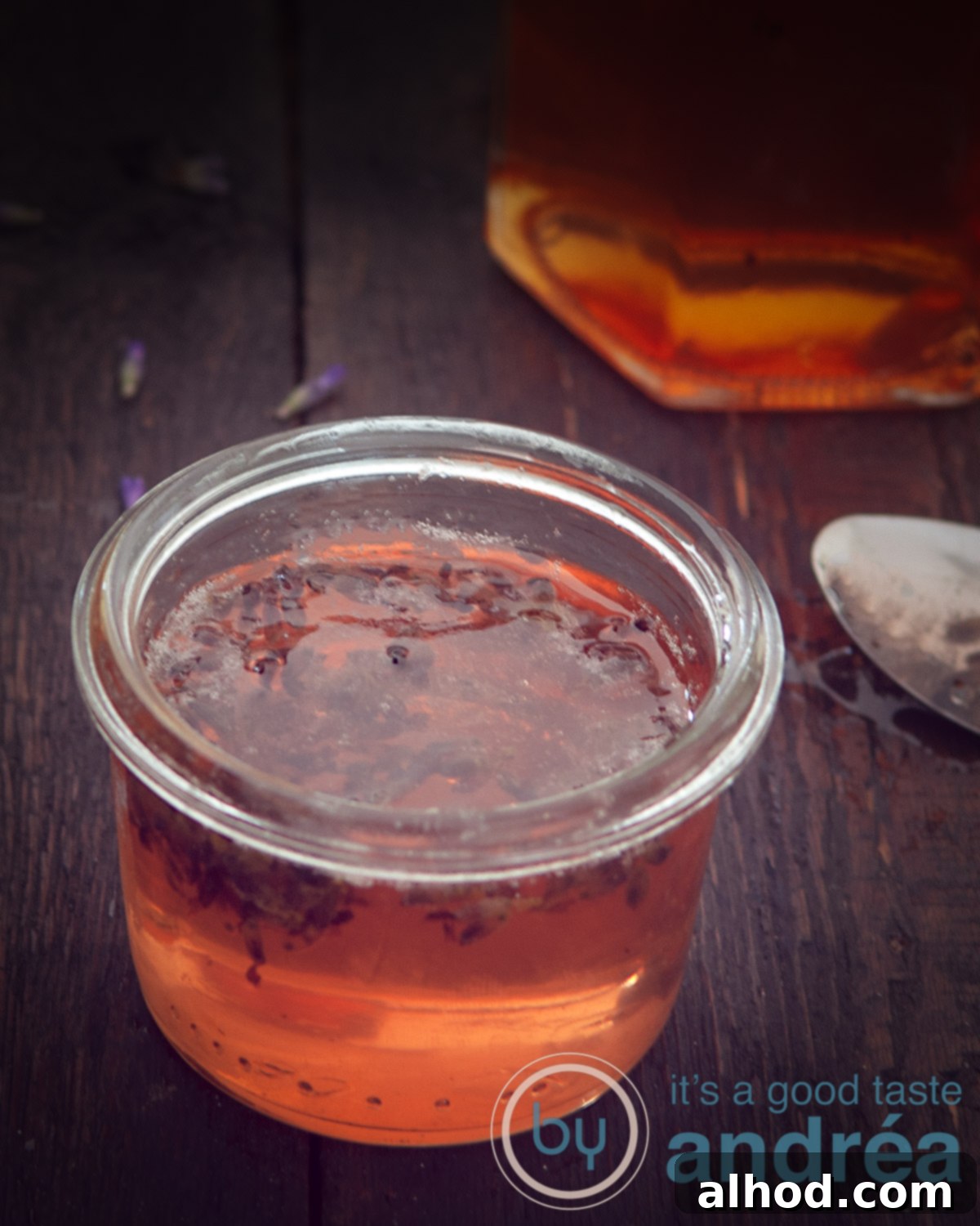 Lavender Kissed Apple Jelly 2 A macro photo of a jar filled with golden apple jelly. A black background highlights its silky texture and inviting caramel color, hinting at a subtle lavender infusion.