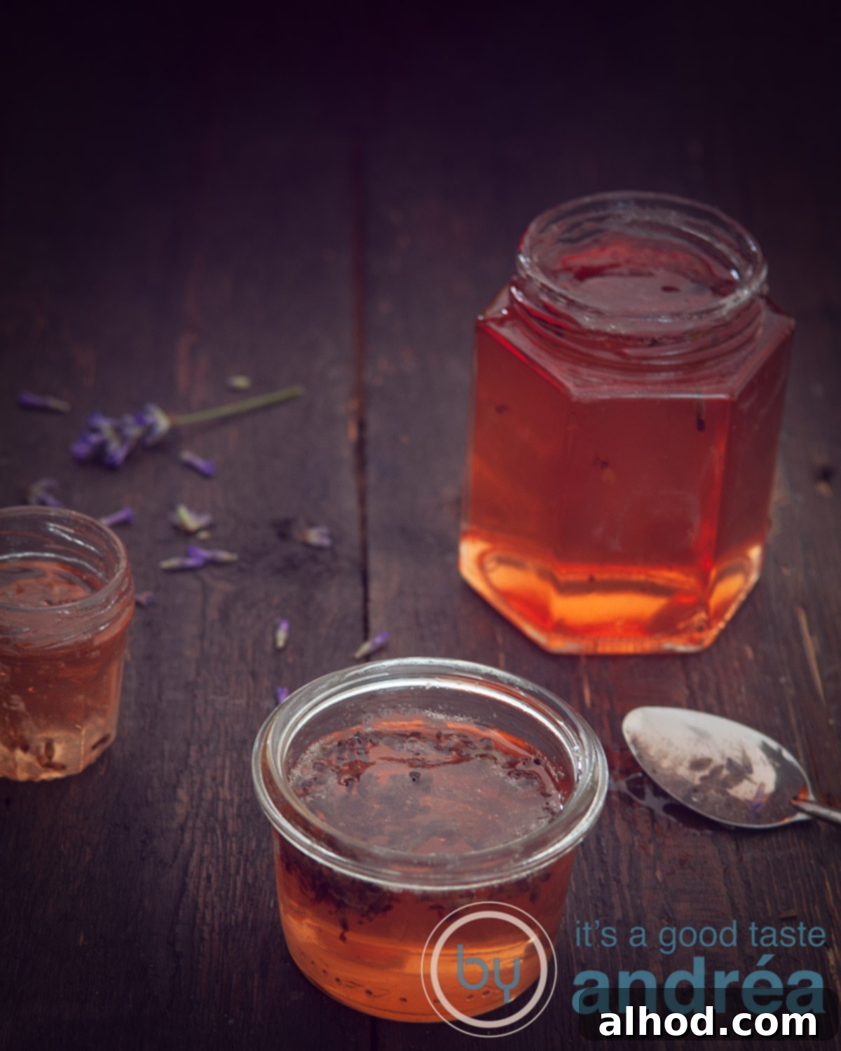 Lavender Kissed Apple Jelly 8 A stunning arrangement of homemade apple jelly with lavender in various glass jars, set against a dark background, highlighting its golden hue and the elegant simplicity of the preserve.