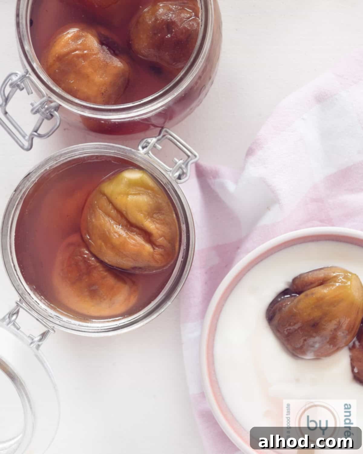The Art of Syruped Figs: Preserving Sweetness 2 Two jars filled with glistening preserved figs in spiced syrup, with a small bowl of yogurt topped with figs and syrup in the foreground, all viewed from above on a rustic surface.