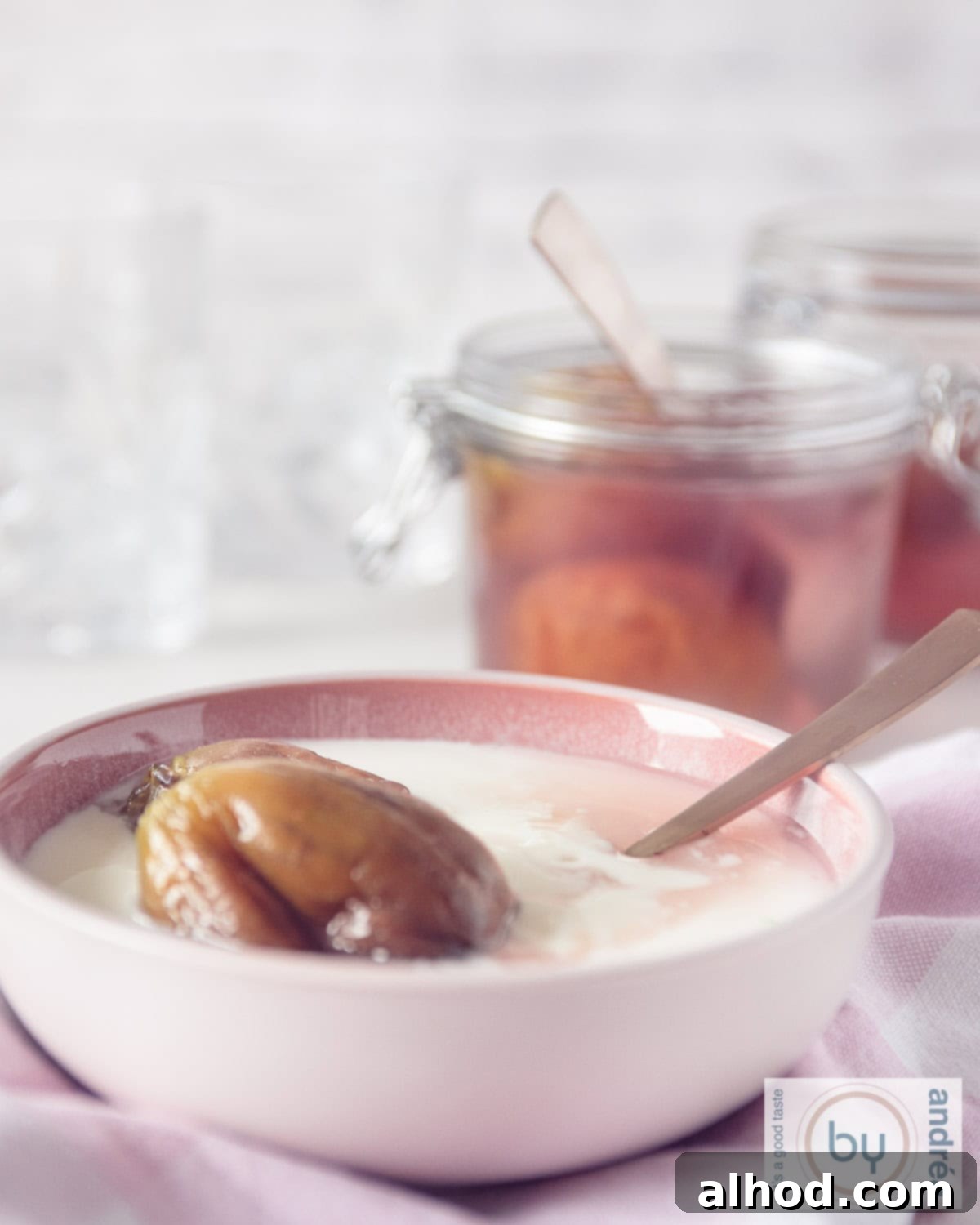 The Art of Syruped Figs: Preserving Sweetness 3 A high-angle shot of a beautiful pink bowl filled with creamy yogurt, generously topped with dark, glistening preserved figs and a drizzle of their rich, spiced syrup. In the softly blurred background, two glass jars containing more figs in syrup hint at a bountiful preserve.