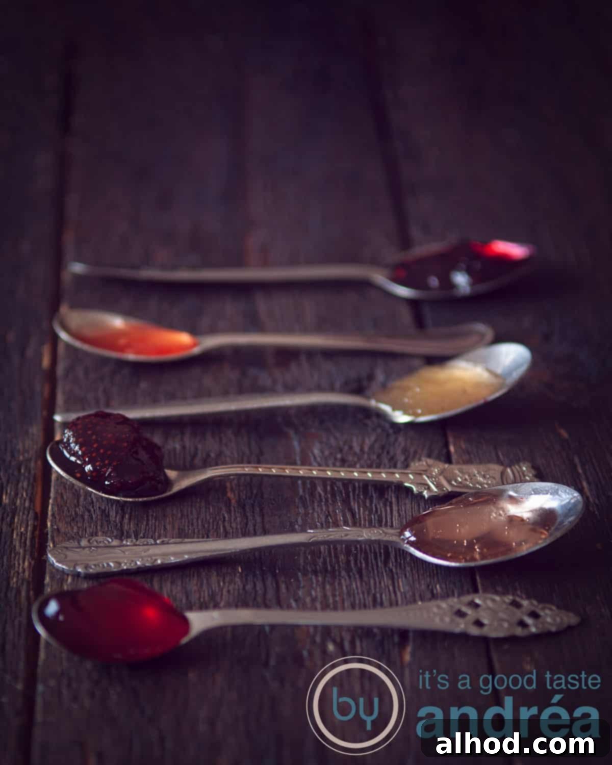 A dark background with 6 spoons filled with different kind of jams, showcasing the variety and rich colors of homemade preserves.