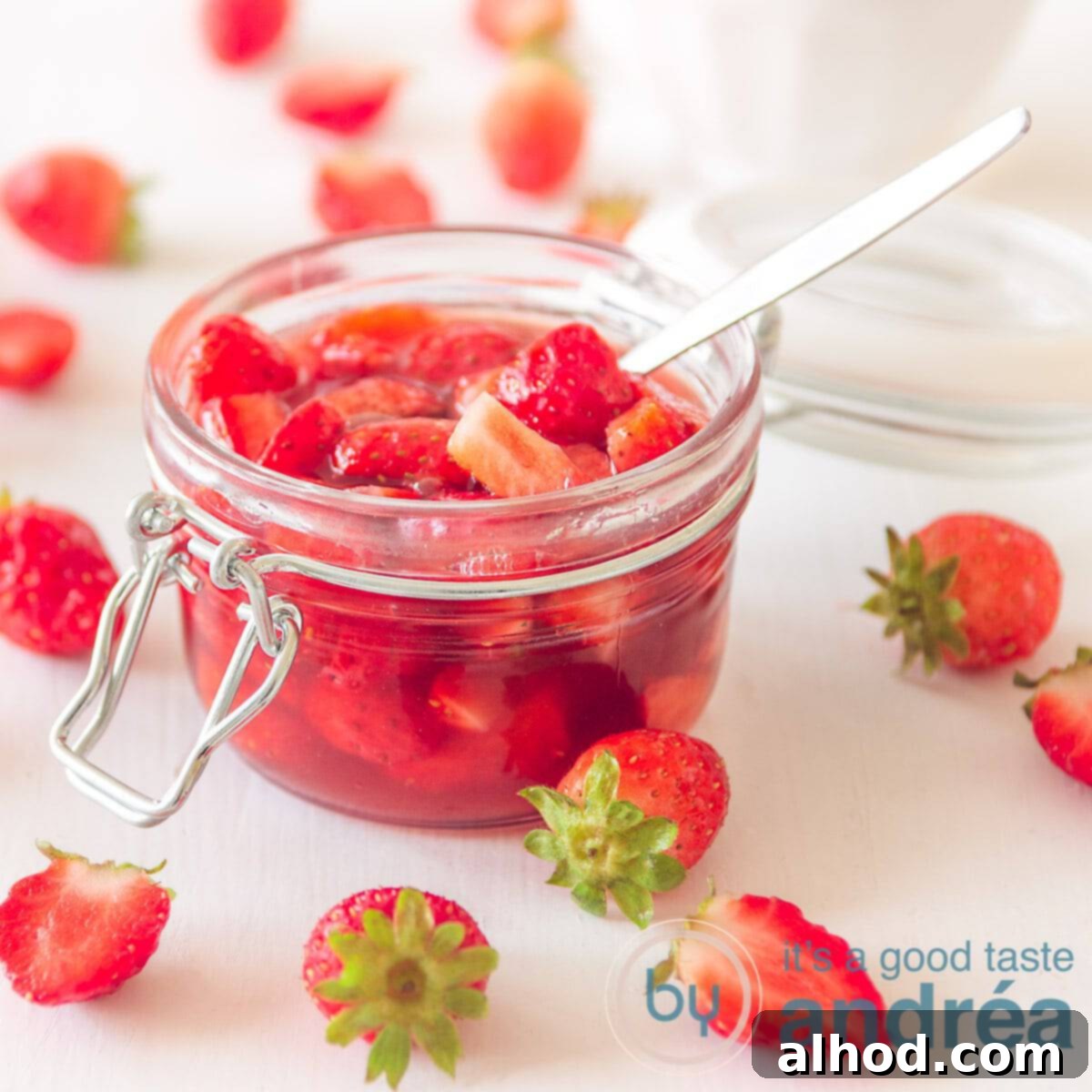a glass jar with strawberry sauce surrounded with strawberries on a white background
