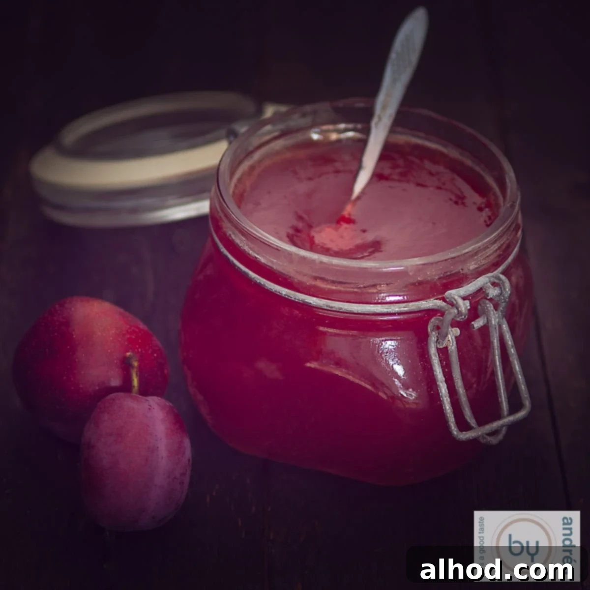 Een vierkante foto van een pot pruimenjam met 2 pruimen aan de zijkant.