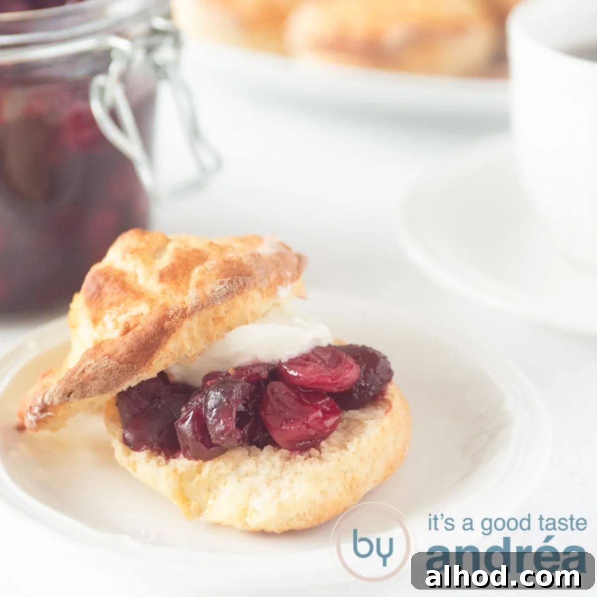 Een vierkante foto met een scone gevuld met clotted cream en cranberry compote. Een witte achtergrond.