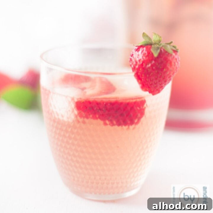 A square photo with a glass of sparkling strawberry lemonade, filled with ice and fresh strawberries, garnished with mint.