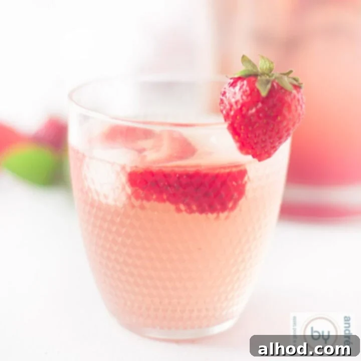 A square photo featuring a vibrant glass of sparkling strawberry lemonade with ice and fresh strawberries in the foreground, ready for sipping.