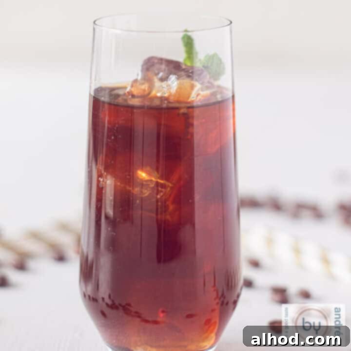 A square photo of a glass filled with Mexican iced coffee, surrounded by coffee beans and straws on a white surface, creating an inviting visual.