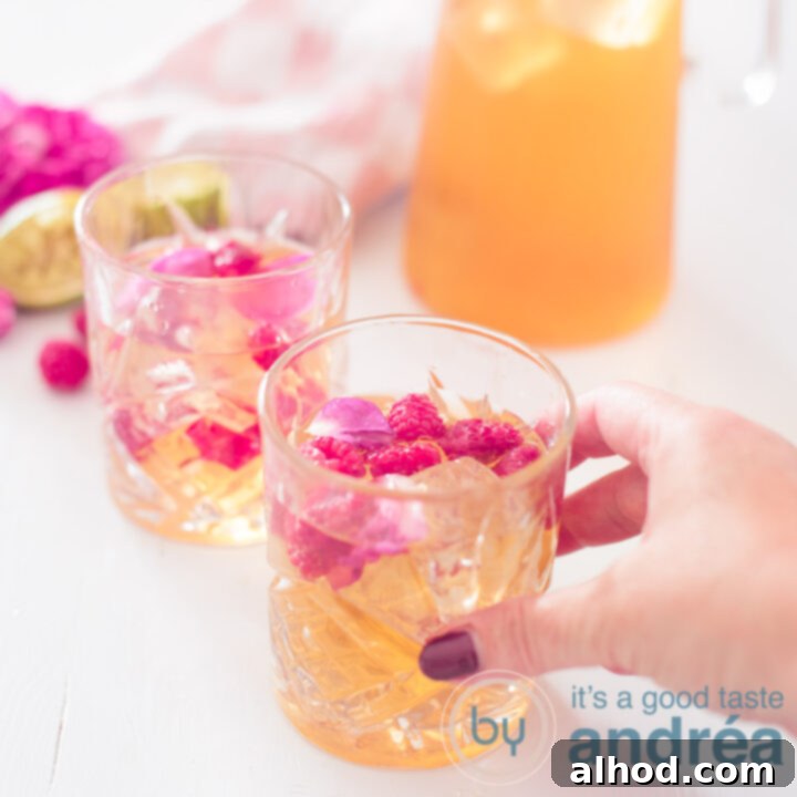 A square picture with lime, rose, and raspberry iced tea in two glasses and a pitcher, with a hand reaching for the first glass against a summer background.