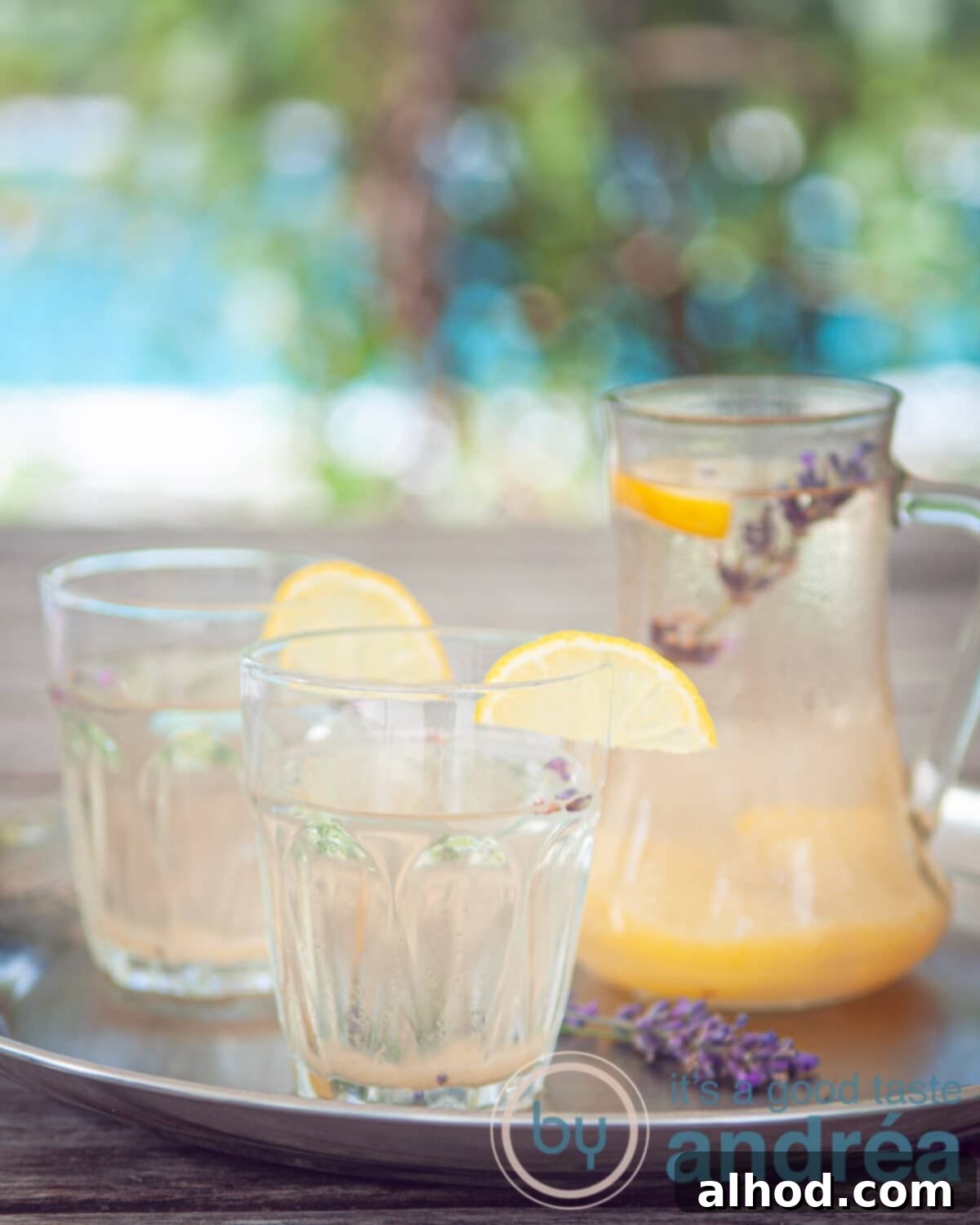 Two glasses of lavender lemonade, garnished with fresh lemon slices and a sprig of lavender, alongside a jar of the lemonade with a summer backdrop.