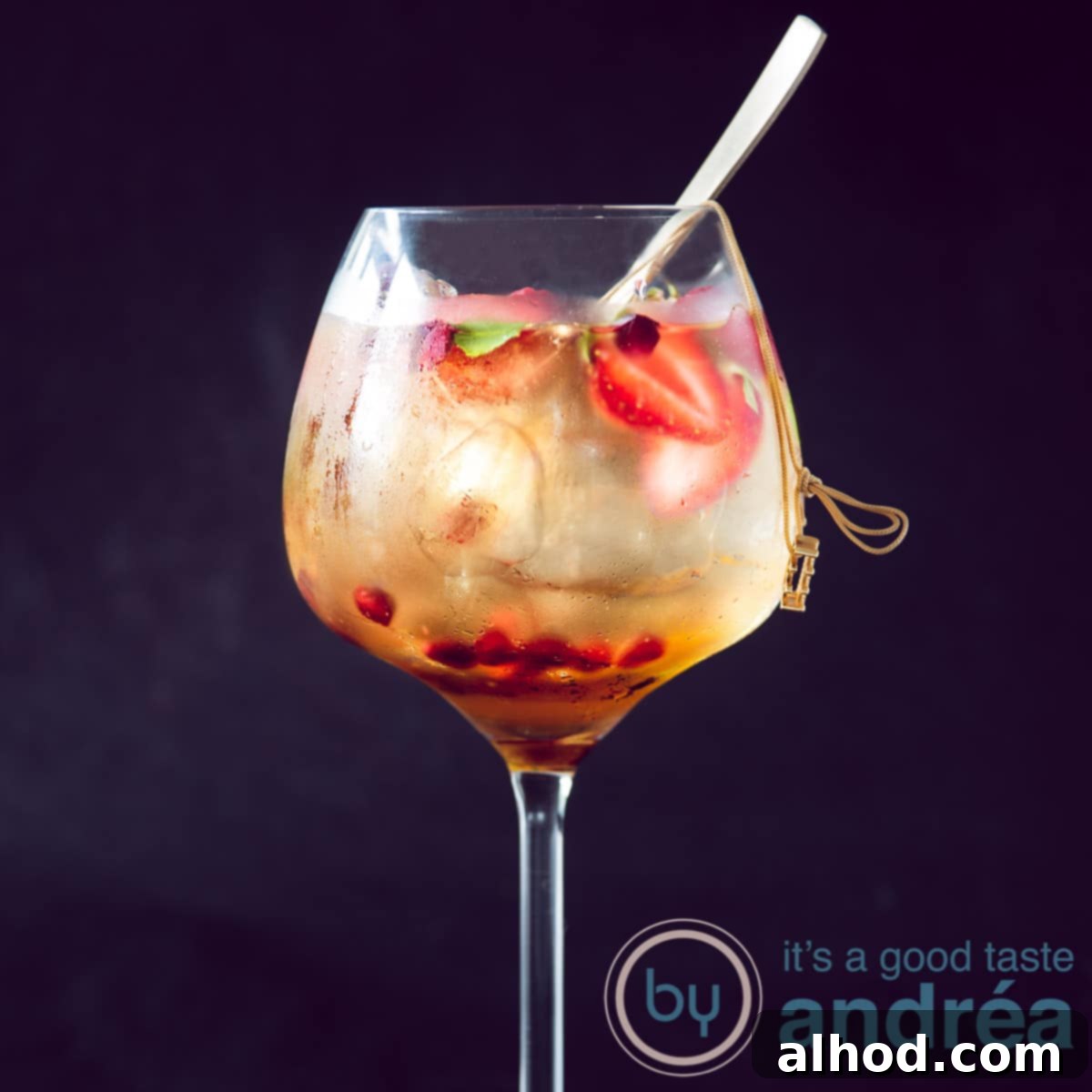 An elegant gin glass filled with Sangria Blanca 43, adorned with fresh fruit, and a golden spoon resting inside, all against a dark, sophisticated background.