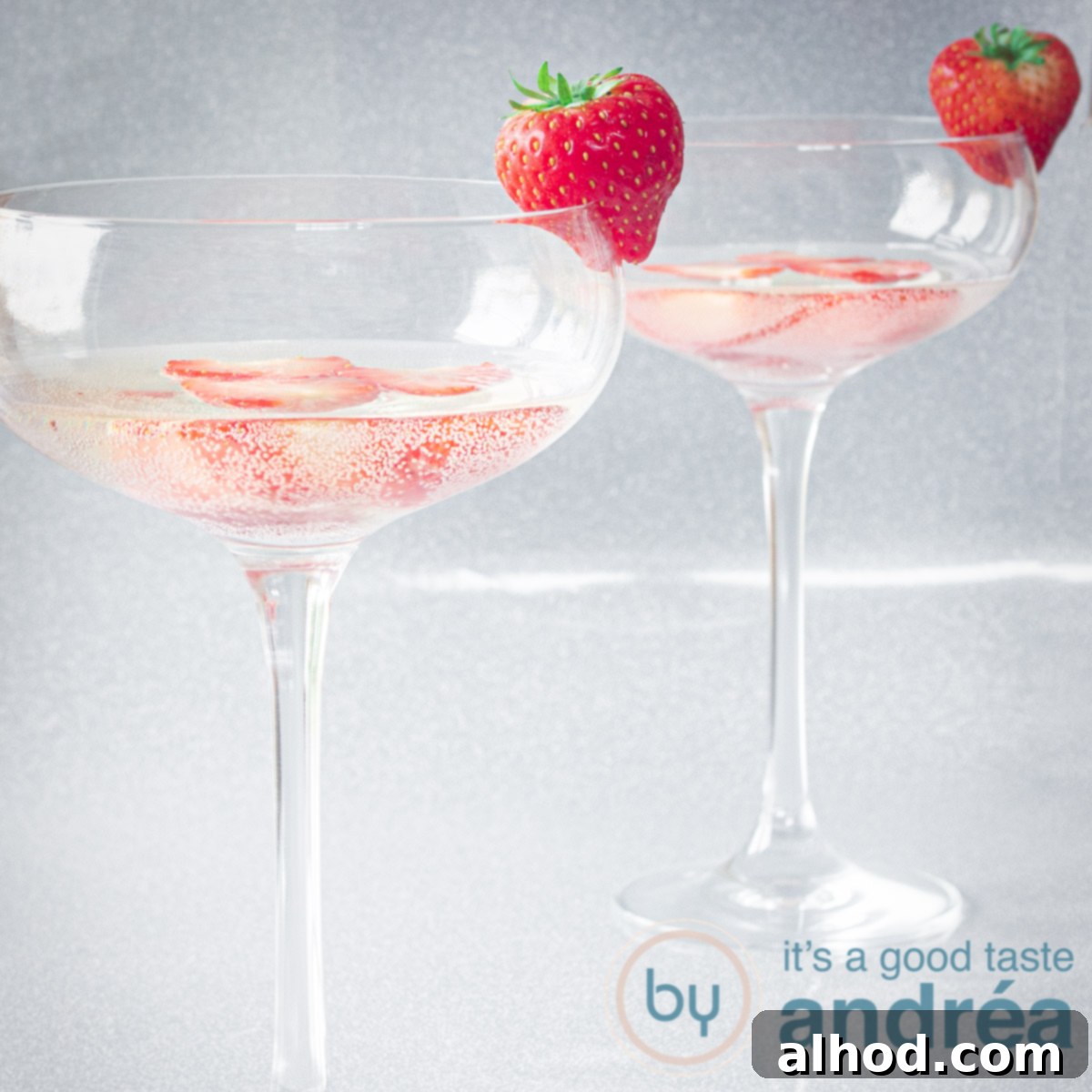 A square photo of two champagne glasses filled with sparkling Prosecco and fresh, ripe strawberries, on a shimmering silver background.