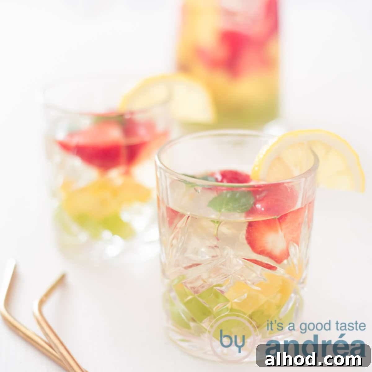A square photo with two glasses filled with white sangria and fresh fruit, beautifully presented on a white background. A hint of golden straws adds a touch of elegance.