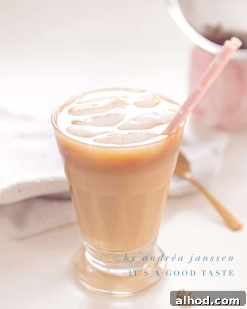 A glass filled with a dirty iced Chai latte, featuring distinct layers and a creamy top, set against a warm background.