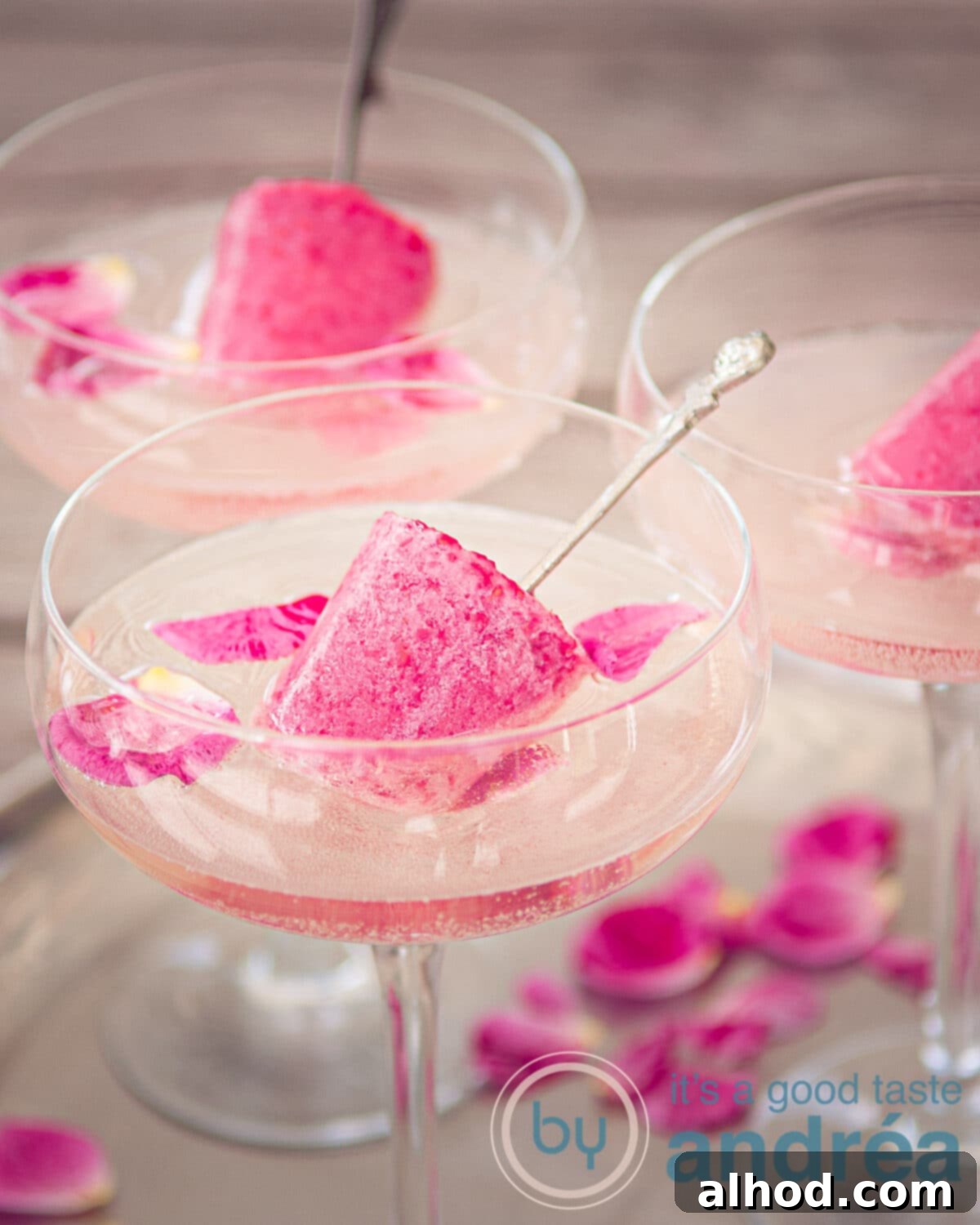 Three elegant champagne glasses holding a celebratory drink with raspberry popsicles and rose petals, presented on a shimmering silver plate.