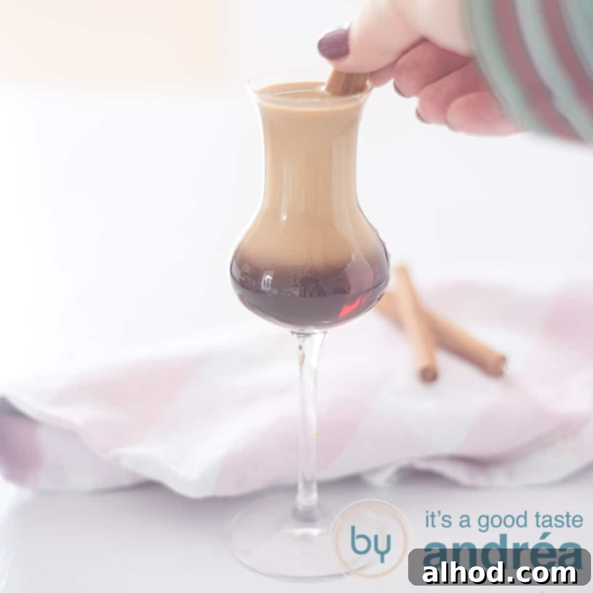 A square photo of a cocktail glass filled with a luxurious Marakesh and Amarula drink, garnished with a cinnamon stick being held by a hand, emphasizing its rich, creamy texture.