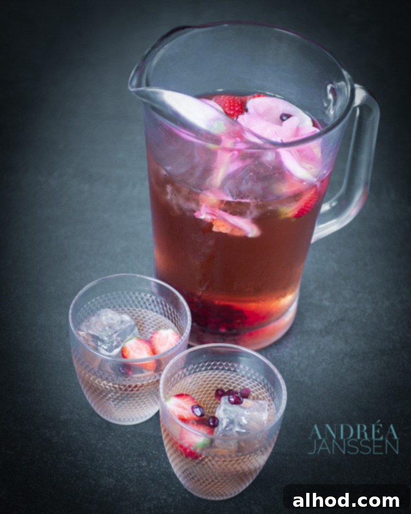 A pitcher of Rose vanilla iced tea, garnished with fresh roses, on a light background.