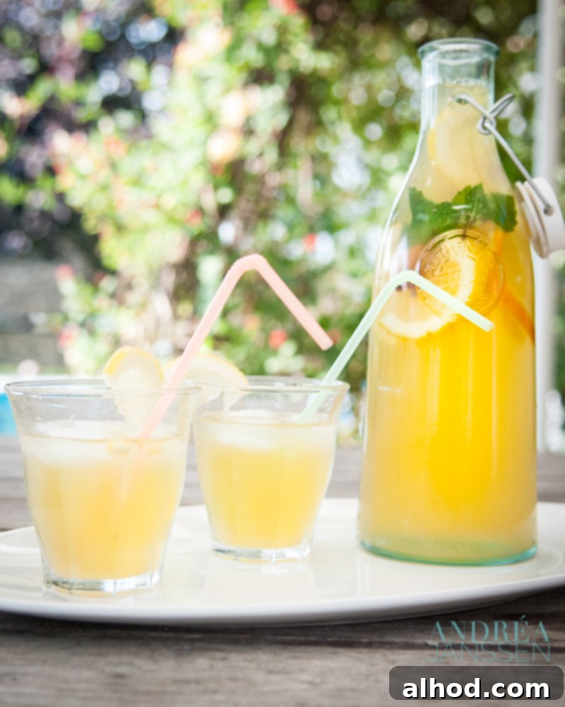 A large pitcher of homemade orange iced tea with slices of orange and lemon, alongside two glasses ready for serving.