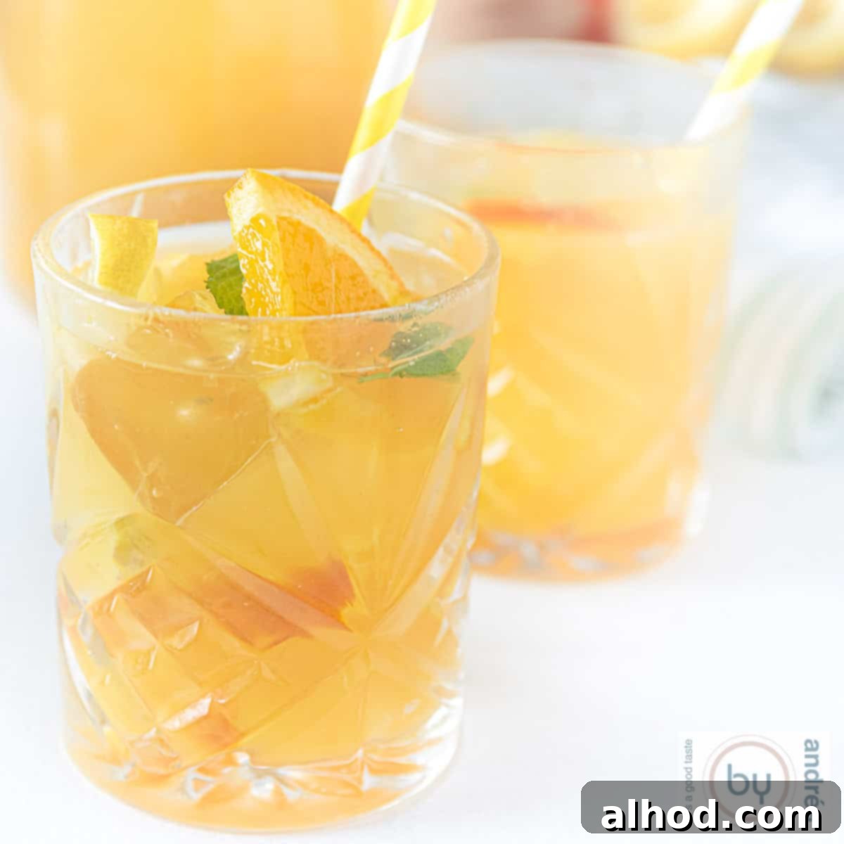 Lemon Mint Cooler 4 A square photo featuring two glasses of refreshing lemon and mint iced tea, garnished with fresh slices of citrus and mint, in front of a glass carafe.