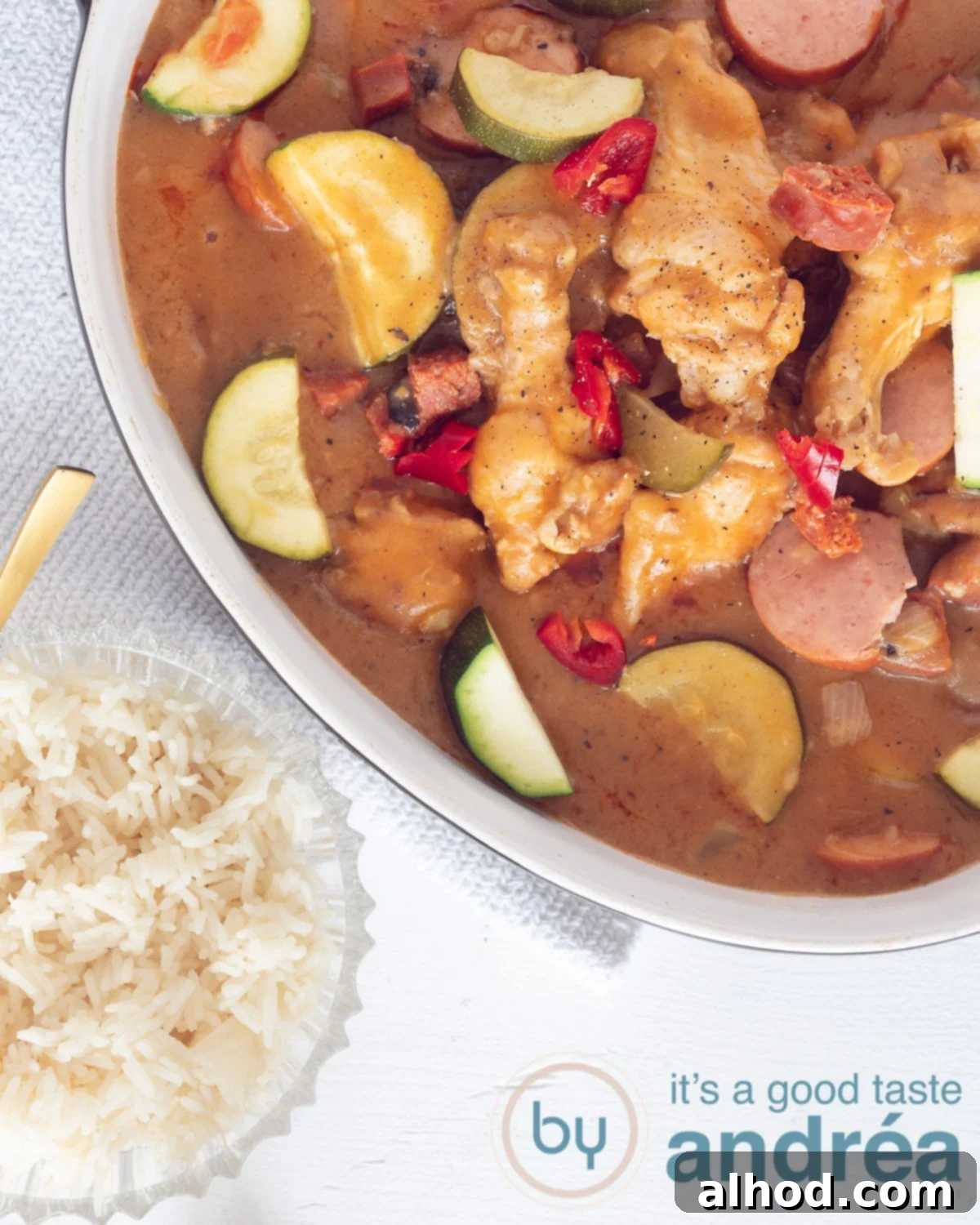 Hearty Cajun Chicken and Sausage Gumbo 3 A pristine white casserole dish brimming with hearty homemade Cajun chicken and sausage gumbo, served alongside a small bowl of perfectly fluffy Louisiana white rice, capturing a scene of comforting Southern cuisine.