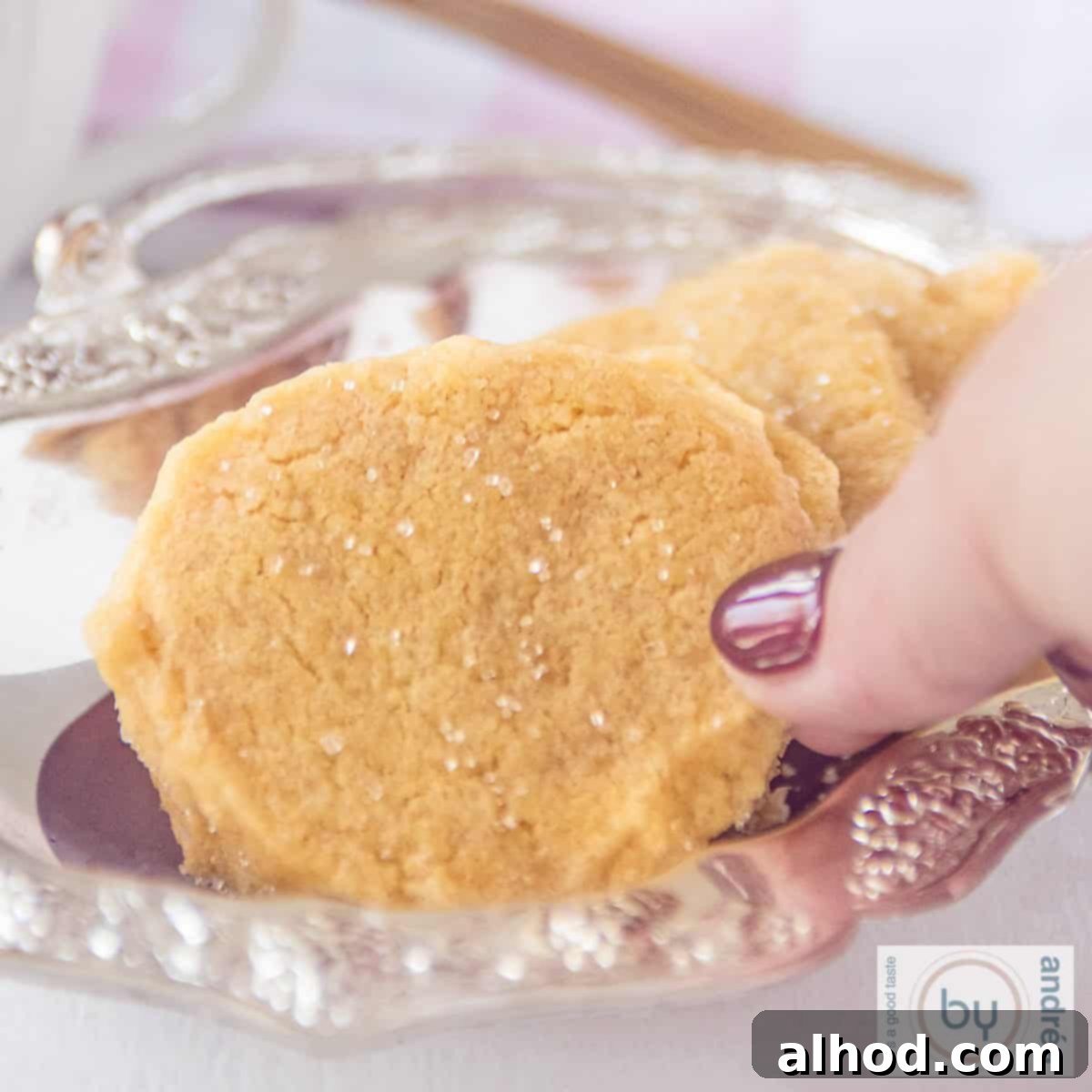 Crisp Ginger Shortbread Delights 6 A square photo showing part of a silver platter with a cookie with a hint of ginger. A hand takes a cookie.