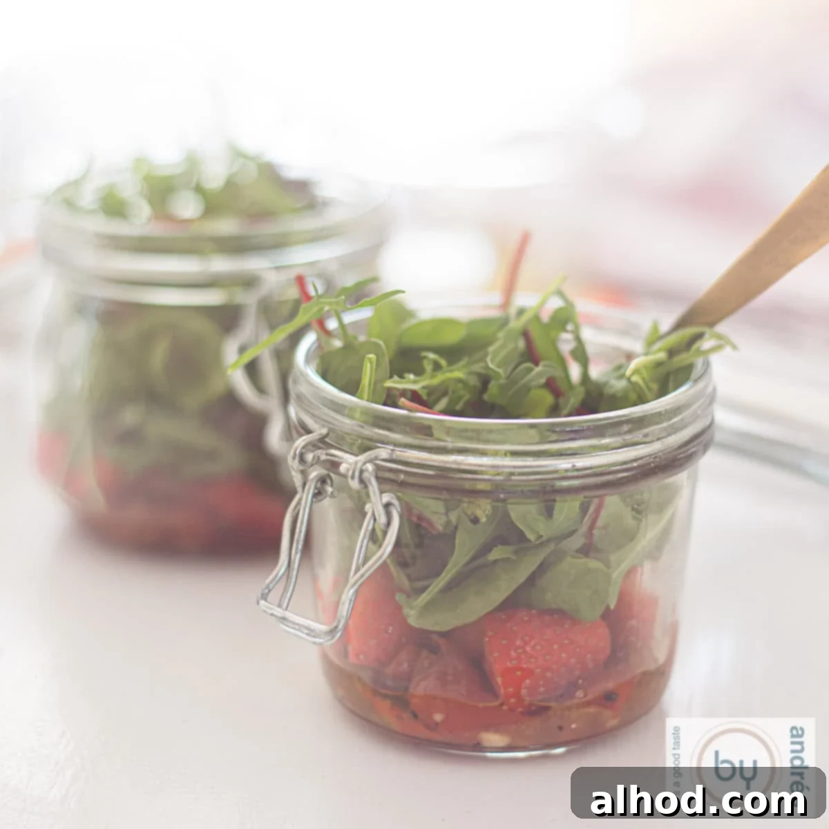 Sunshine in a Jar Salads 3 A square picture with two jars filled with fresh salad with lettuce, strawberries and honey mustard dressing