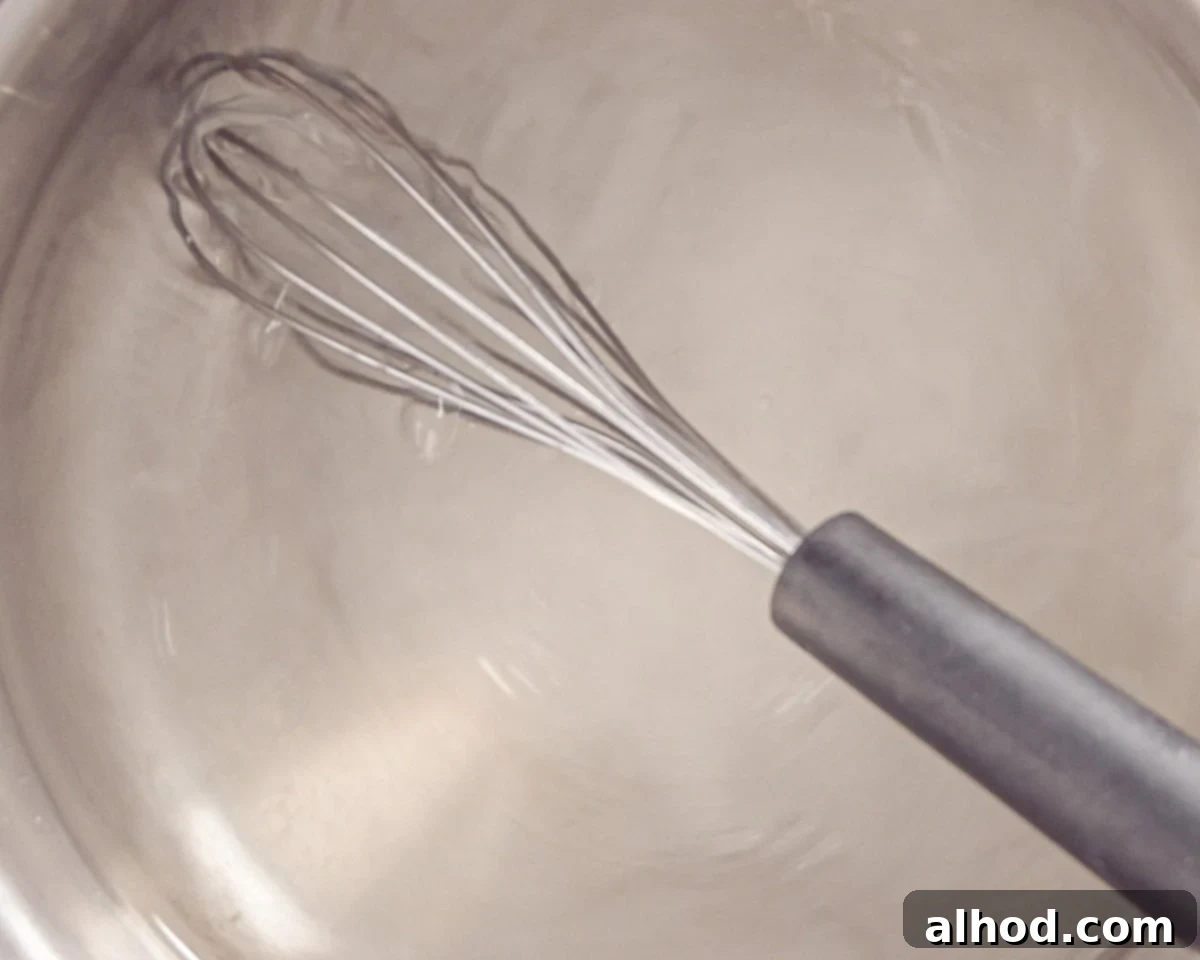 A hand whisking sugar and hot water in a saucepan to create a simple syrup.
