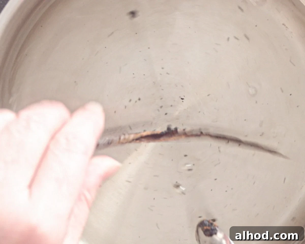A vanilla pod being placed into the warm sugar water in a saucepan.