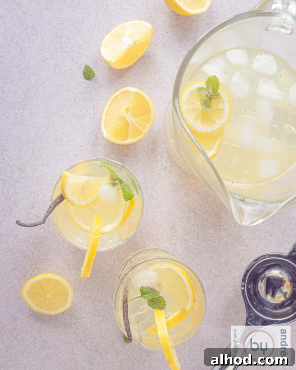 A top-down height photo featuring two glasses of vanilla lemonade garnished with lemon and mint, alongside a pitcher of lemonade and scattered lemon slices.
